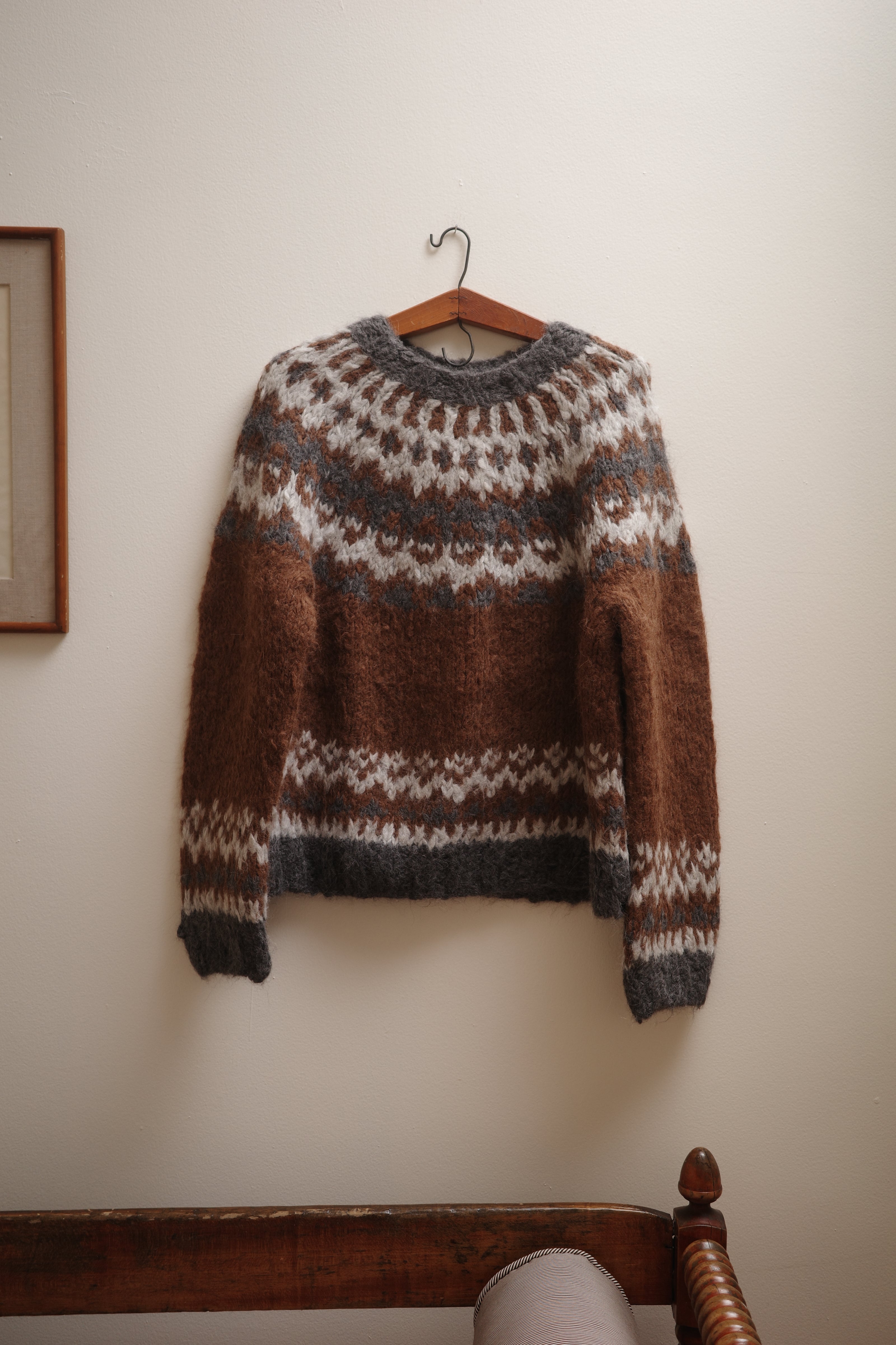 Brown and gray patterned sweater on a wooden hanger against a white wall.