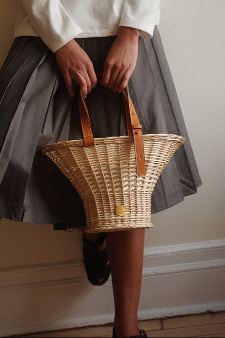 Person wearing a white long-sleeve shirt and gray skirt holding a woven basket.