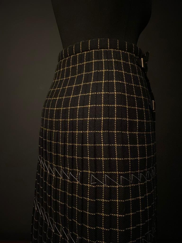 The behind view of a mannequin dressed in a black and yellow plaid kilt in front of a dark backdrop