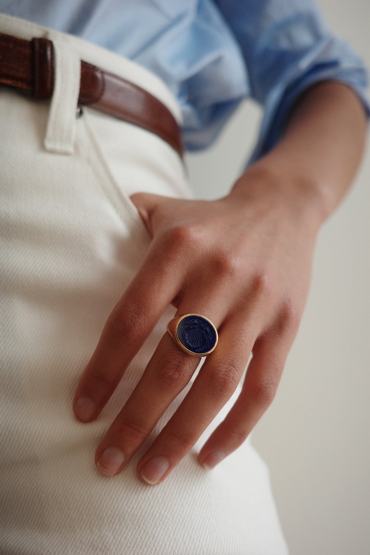 Hand wearing a ring with a blue stone on a neutral background
