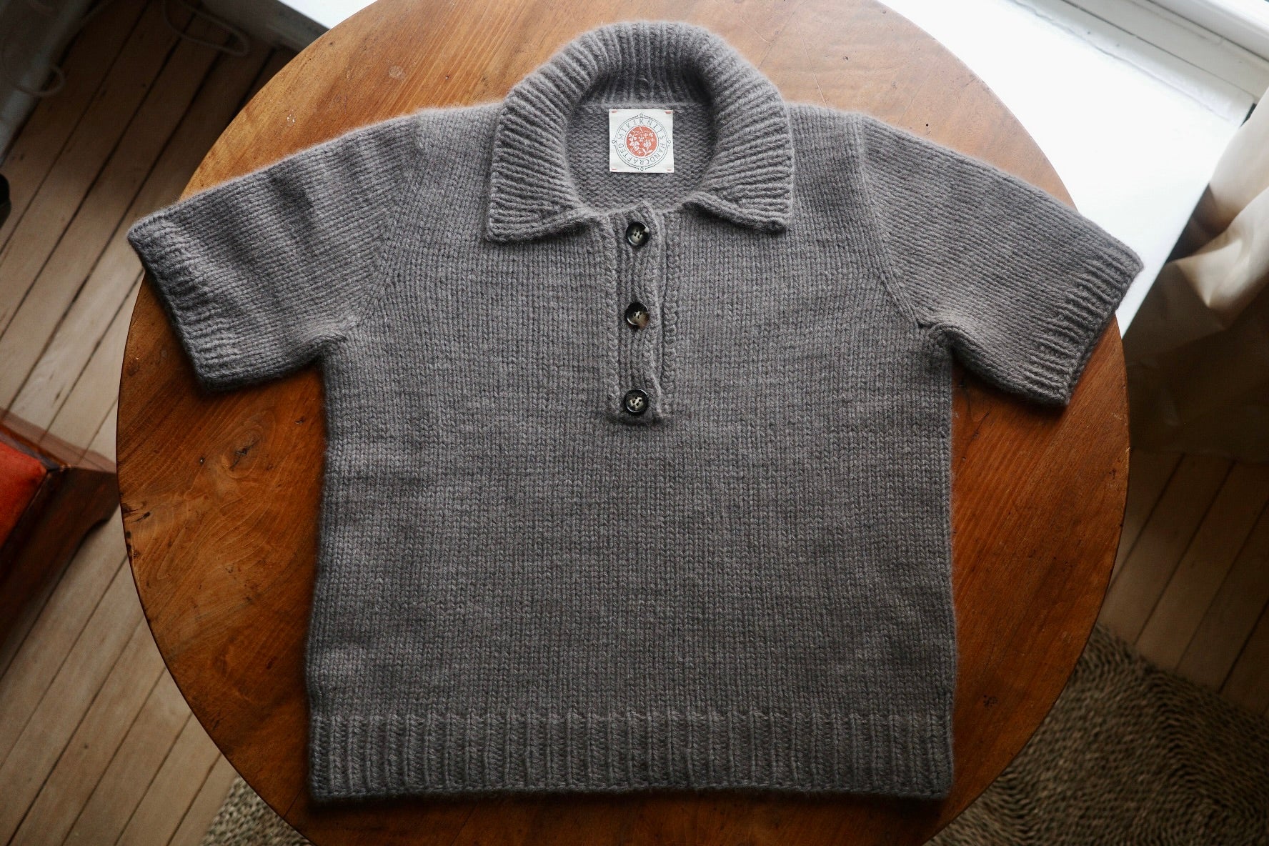 A aupe colored short sleeved sweater lays flat on a wooden table