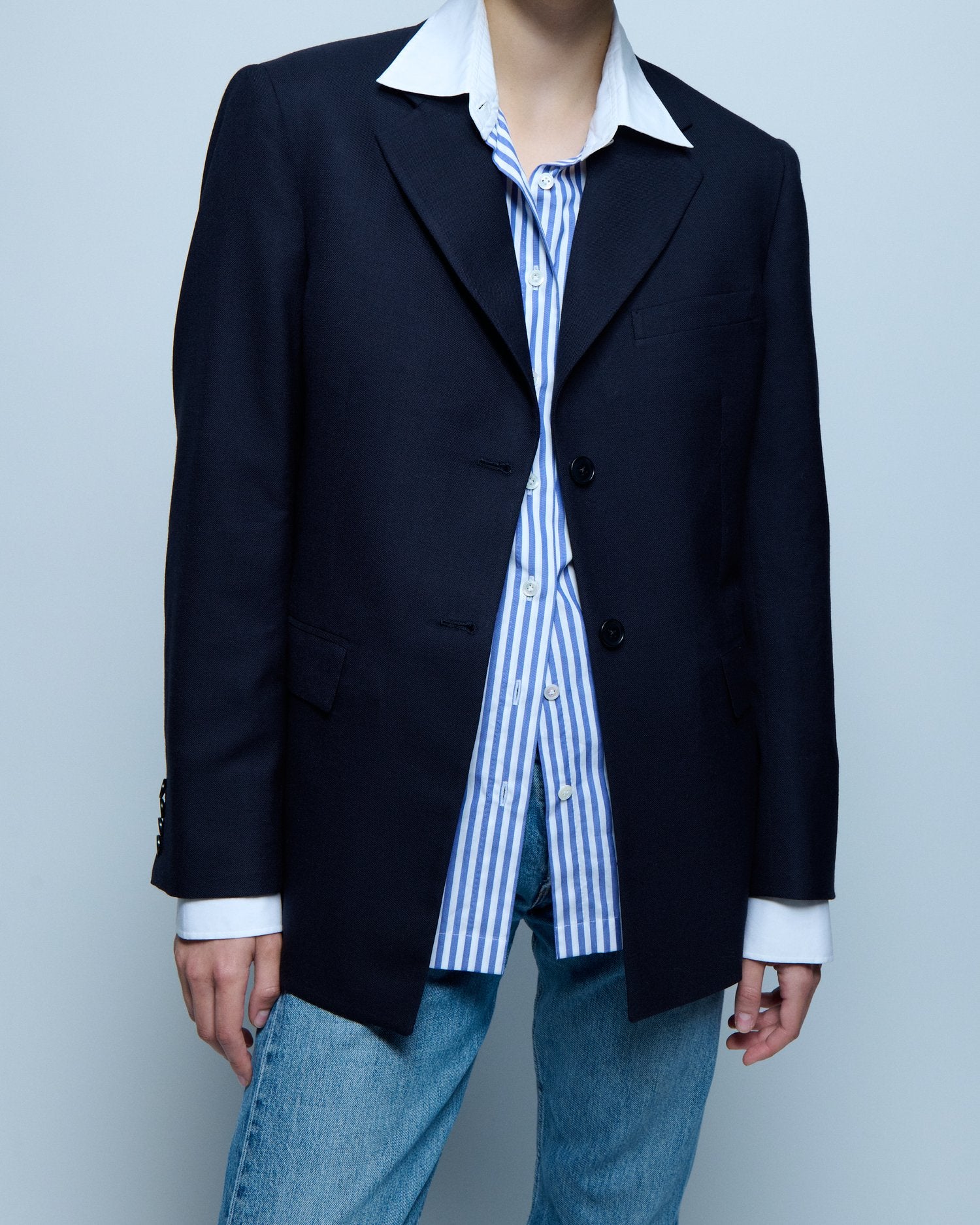 A cropped image of a model wearing a blue blazer with a striped white and blue button down shirt underneath.