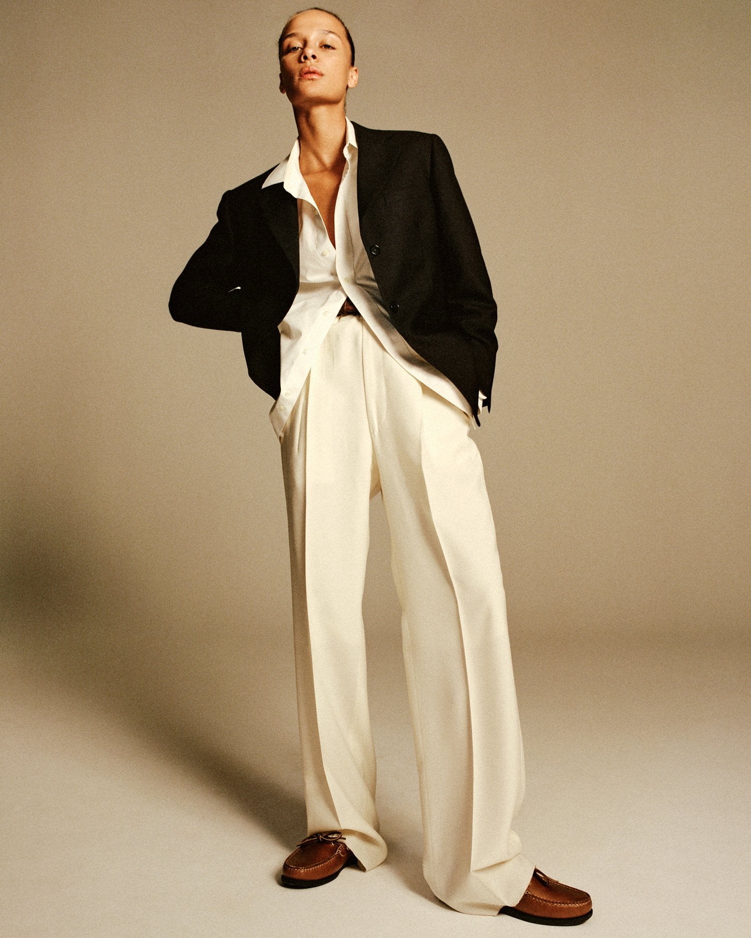A model stands posing with her hand on her hip wearing pleated white trousers and a black blazer.
