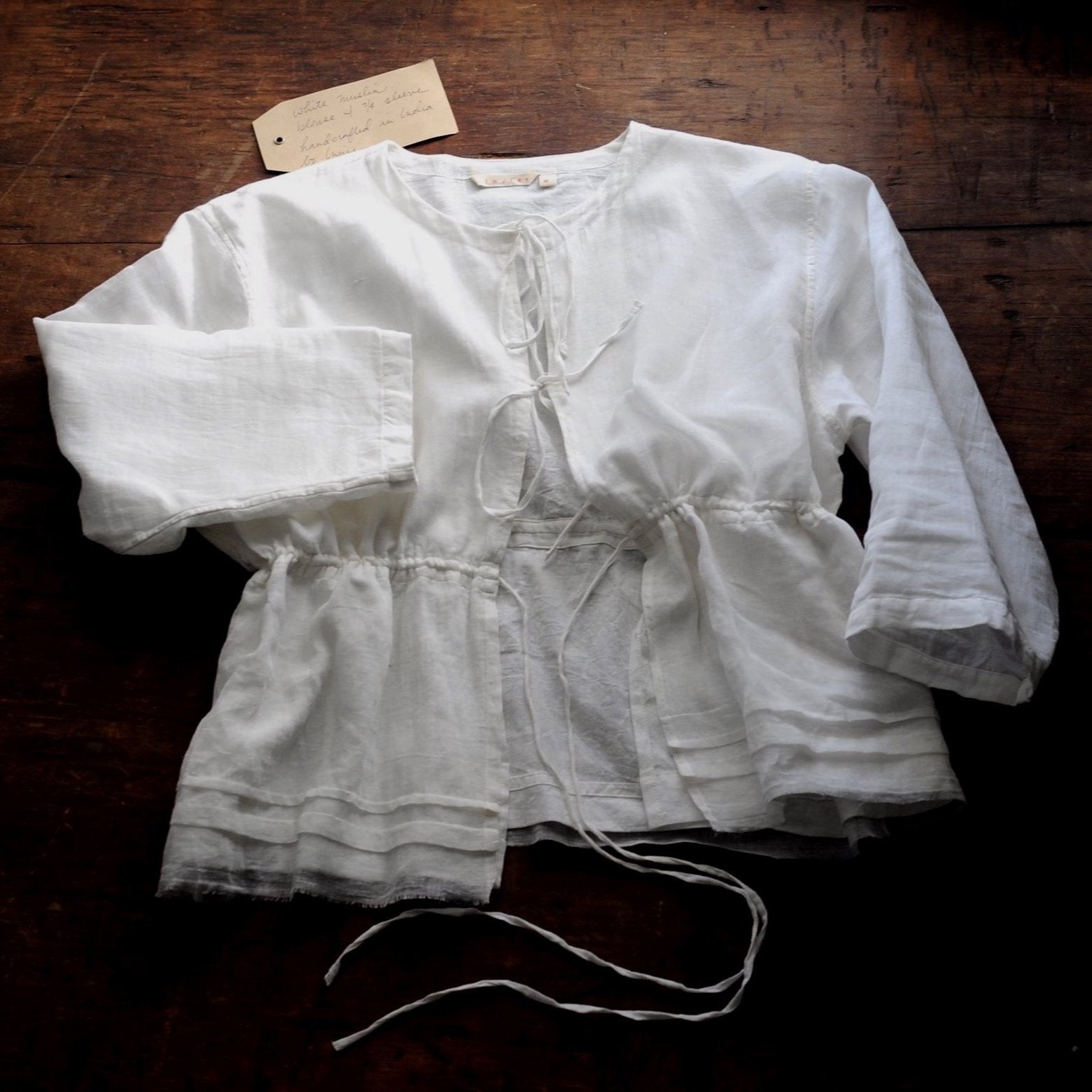 A white top with bow ties lays flat on top of a wooden table.
