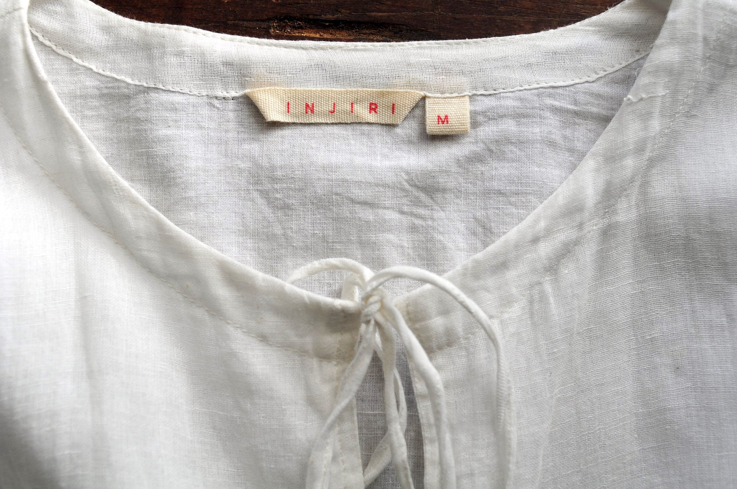 Close up image of the neck opening of a white chemise top with a label reading &