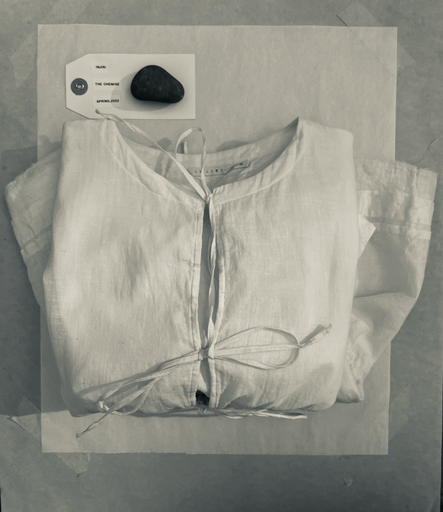 A folded chemise with delicate bow accents sits folded on top of white tissue paper next to a tag that reads. &