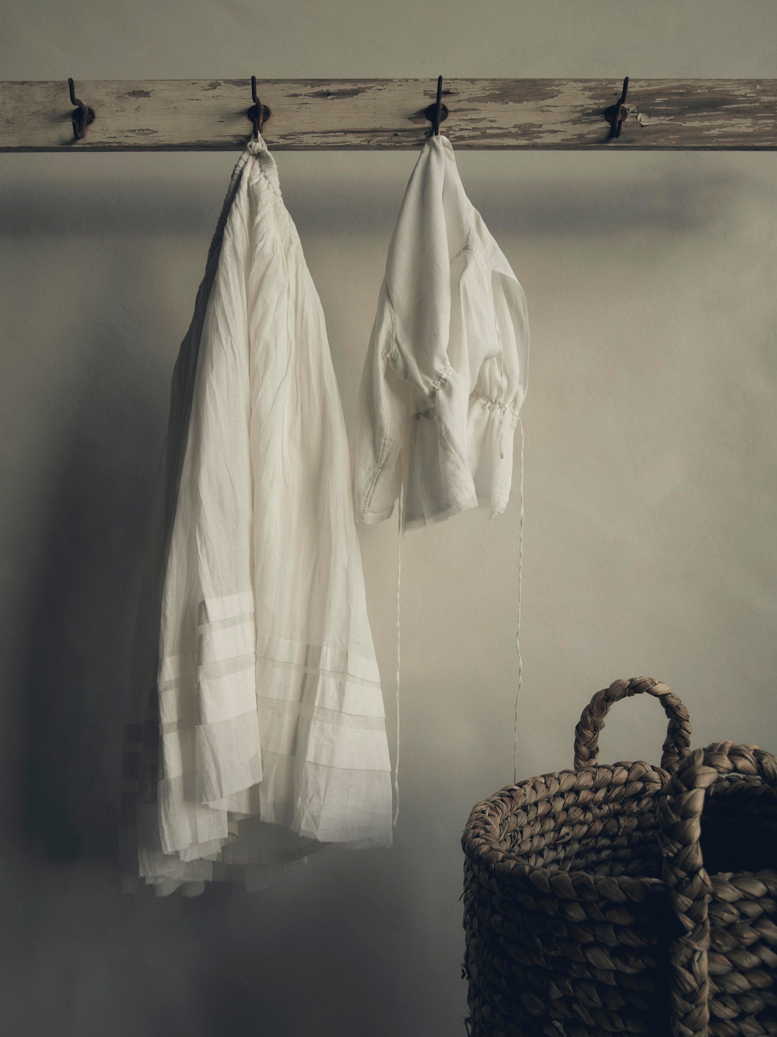 A white petticoat and matching white blouse hang side by side on iron hooks above a wicker basket.