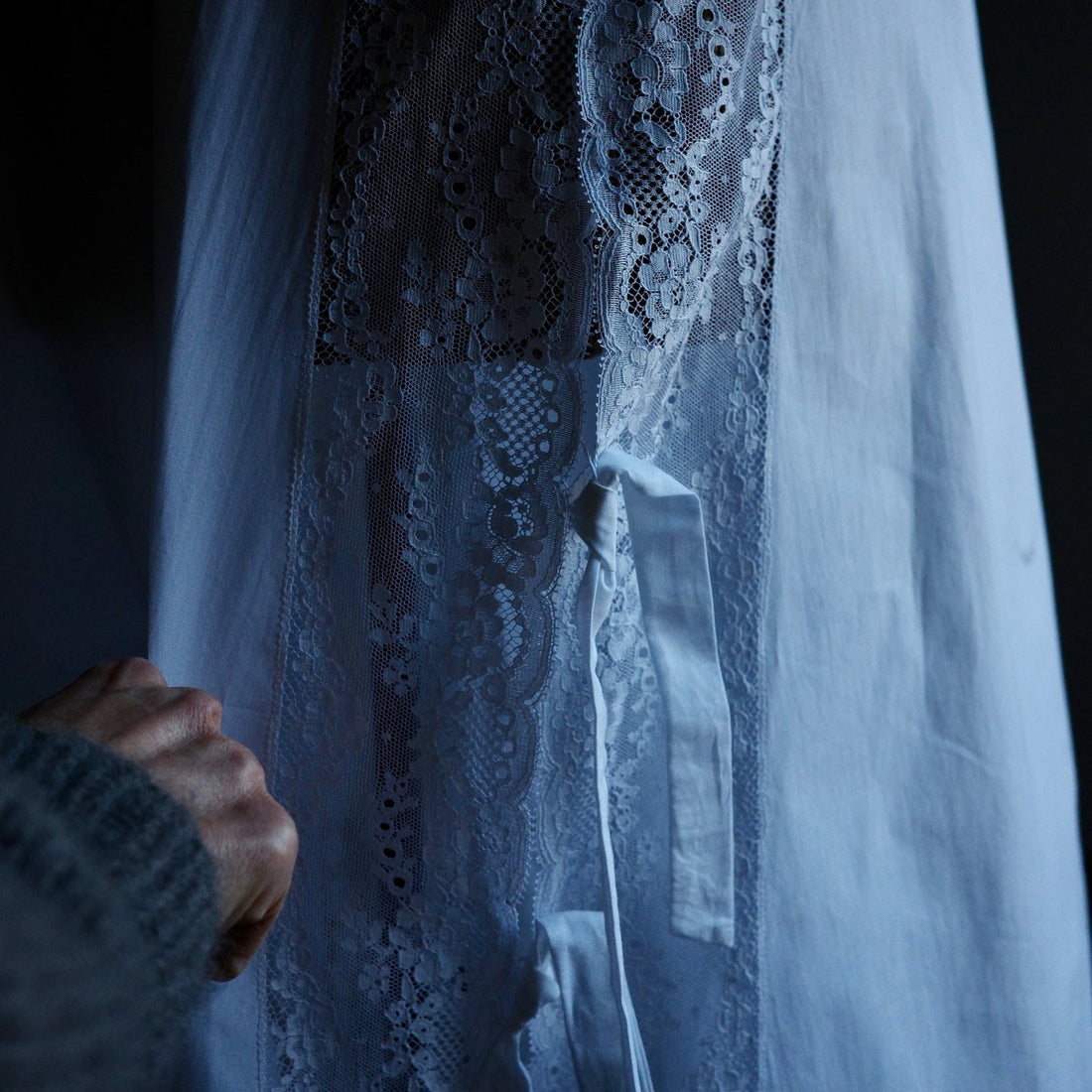 Lace detailing on a white skirt with a hand sewing.