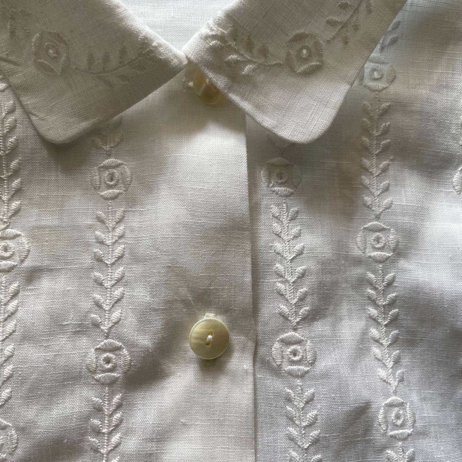 Close up image of floral embroidery on a white shirt with buttons and collar.
