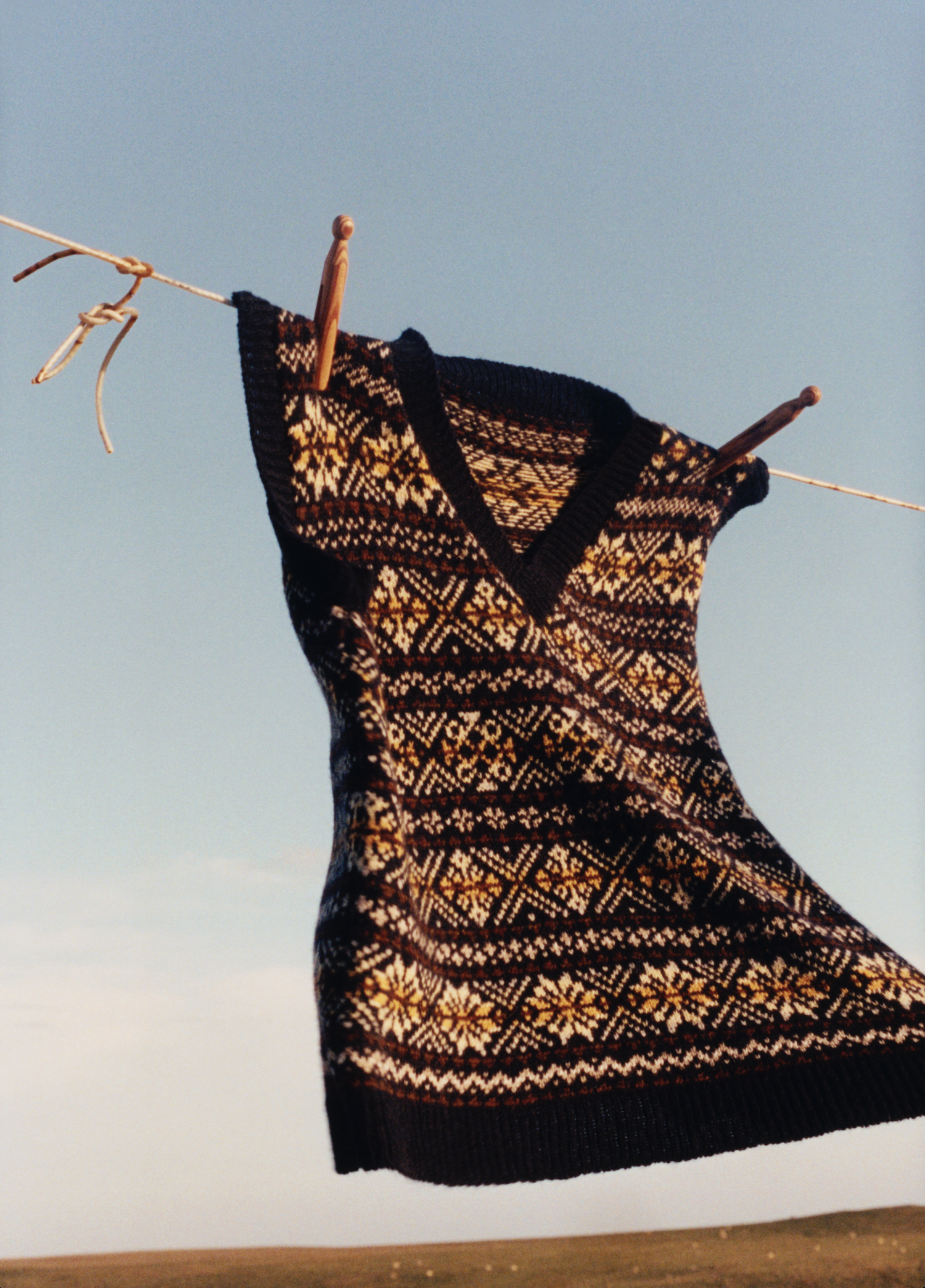A traditional Fair Isle vest hanging on a clothesline against a blue sky.