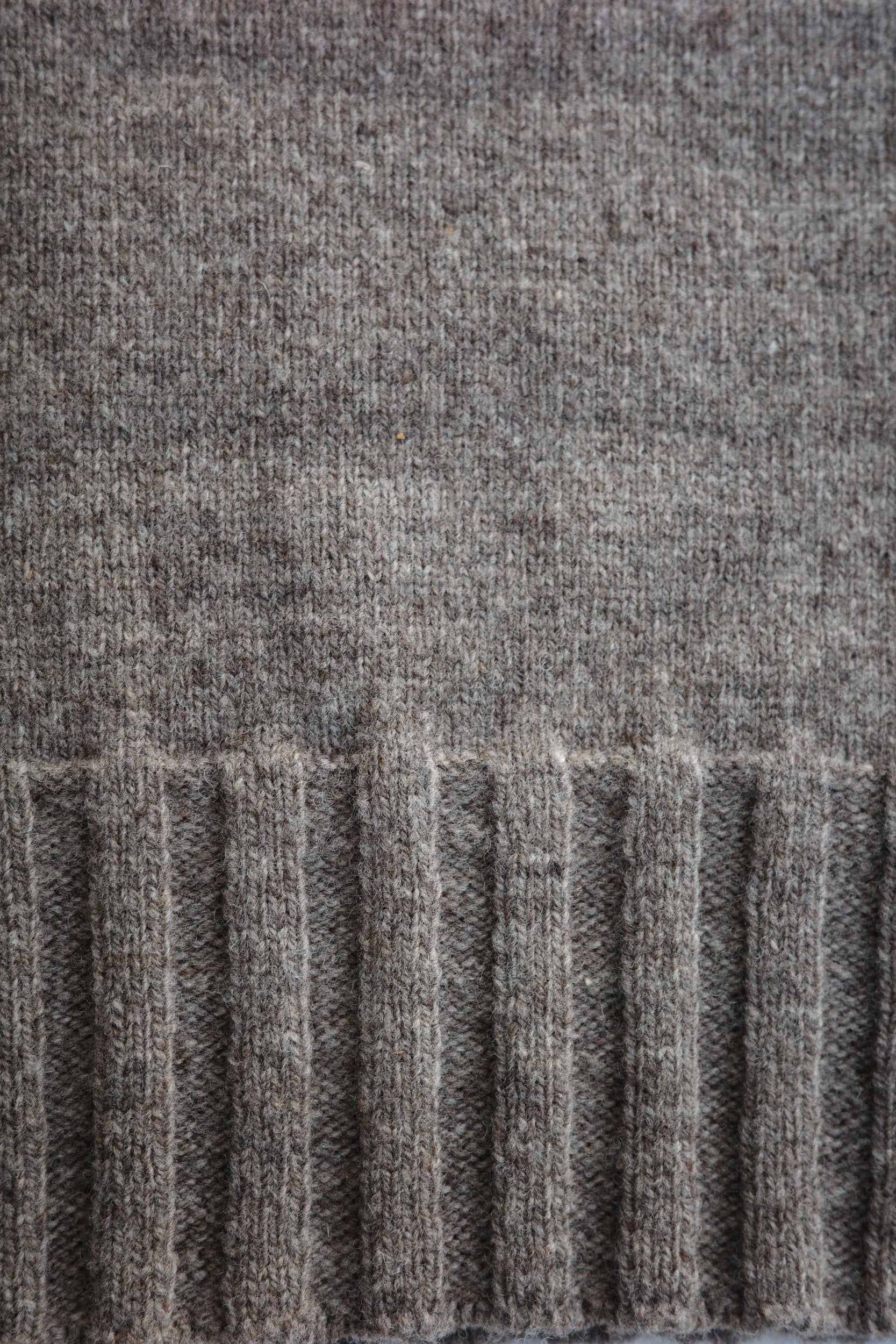 Rib detailing on the bottom of a grey sweater.