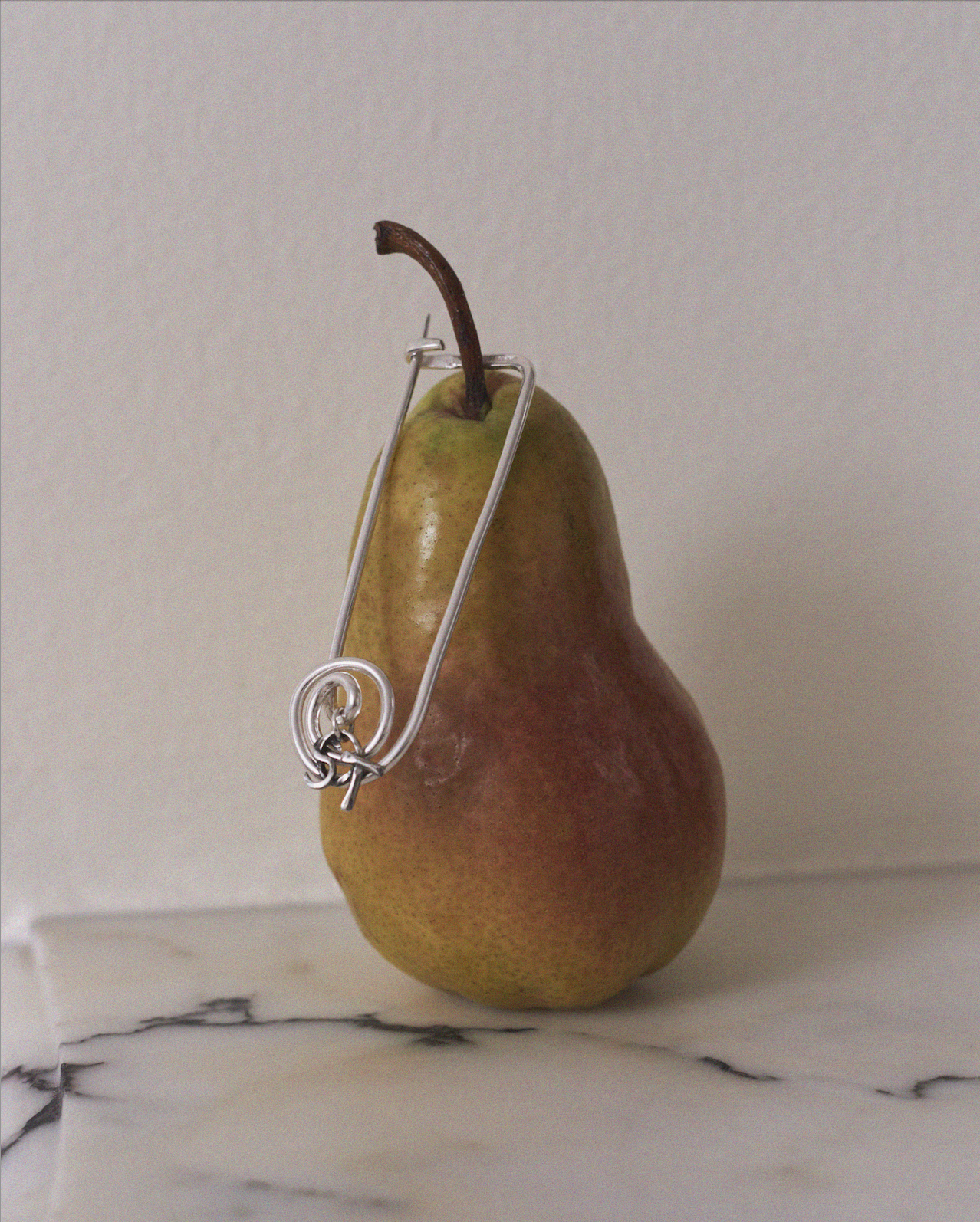 Pear with a silver wire wrapped around it on a marble surface