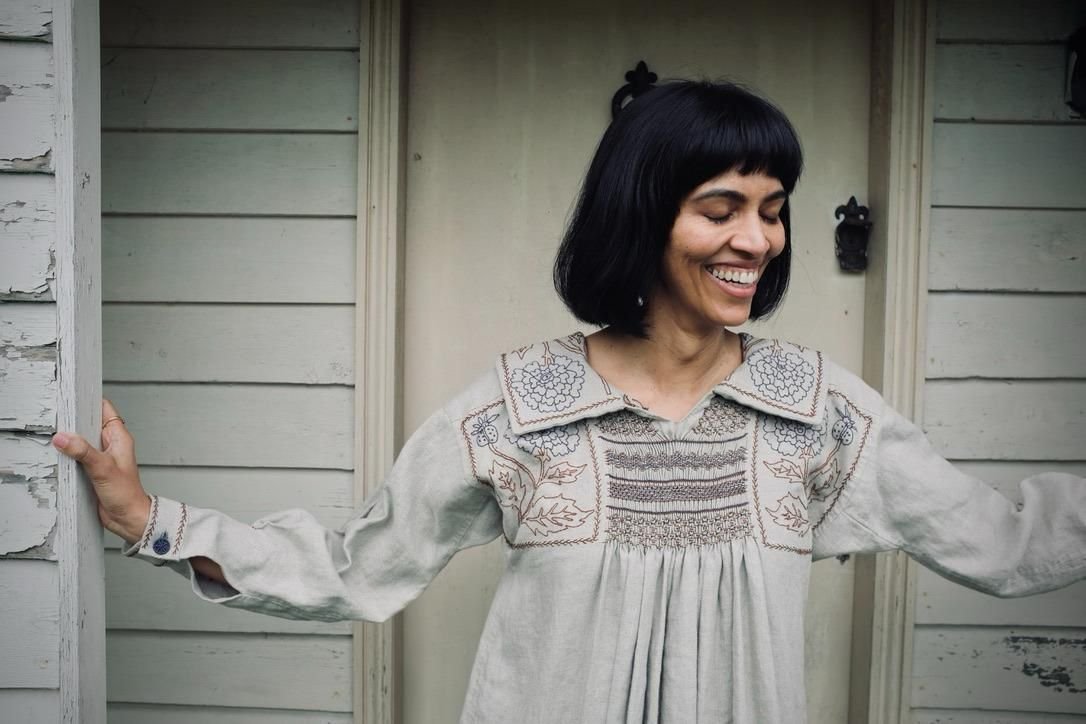 A woman laughing wearing an embroidered dress.