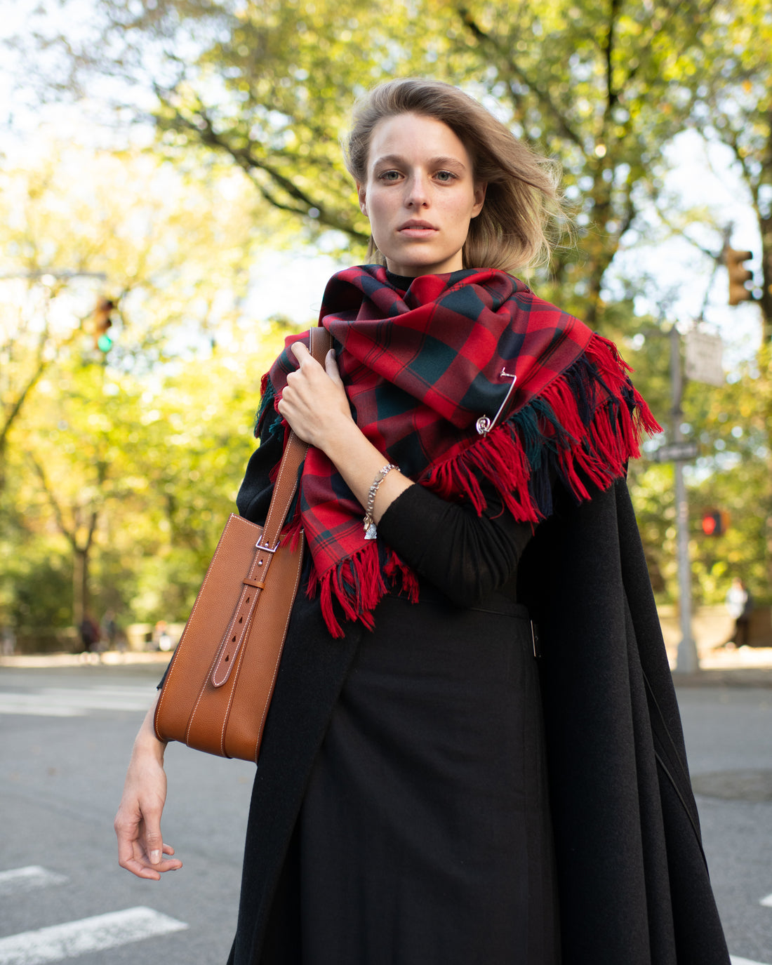 Woman wearing a red and black plaid scarf outdoors on a street.