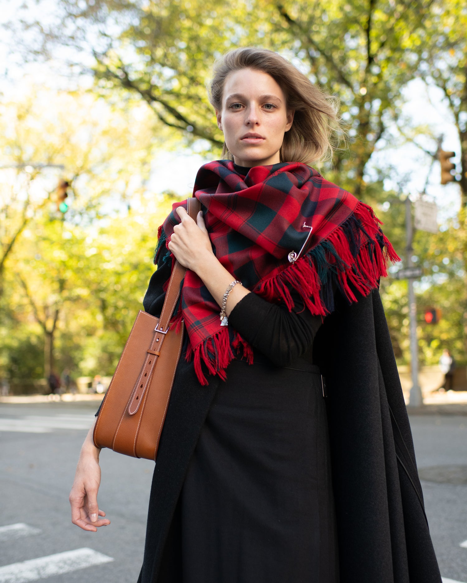 Woman wearing a red and black plaid scarf outdoors on a street.