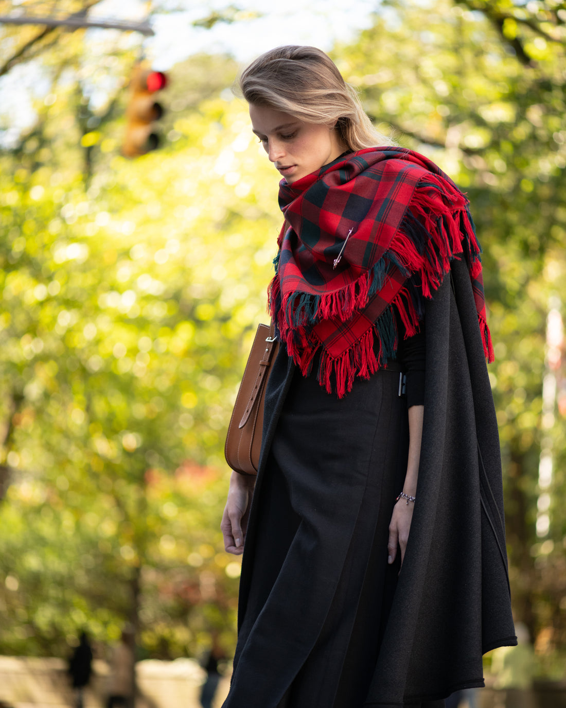 Woman wearing a red and black checkered scarf outdoors with blurred greenery in the background