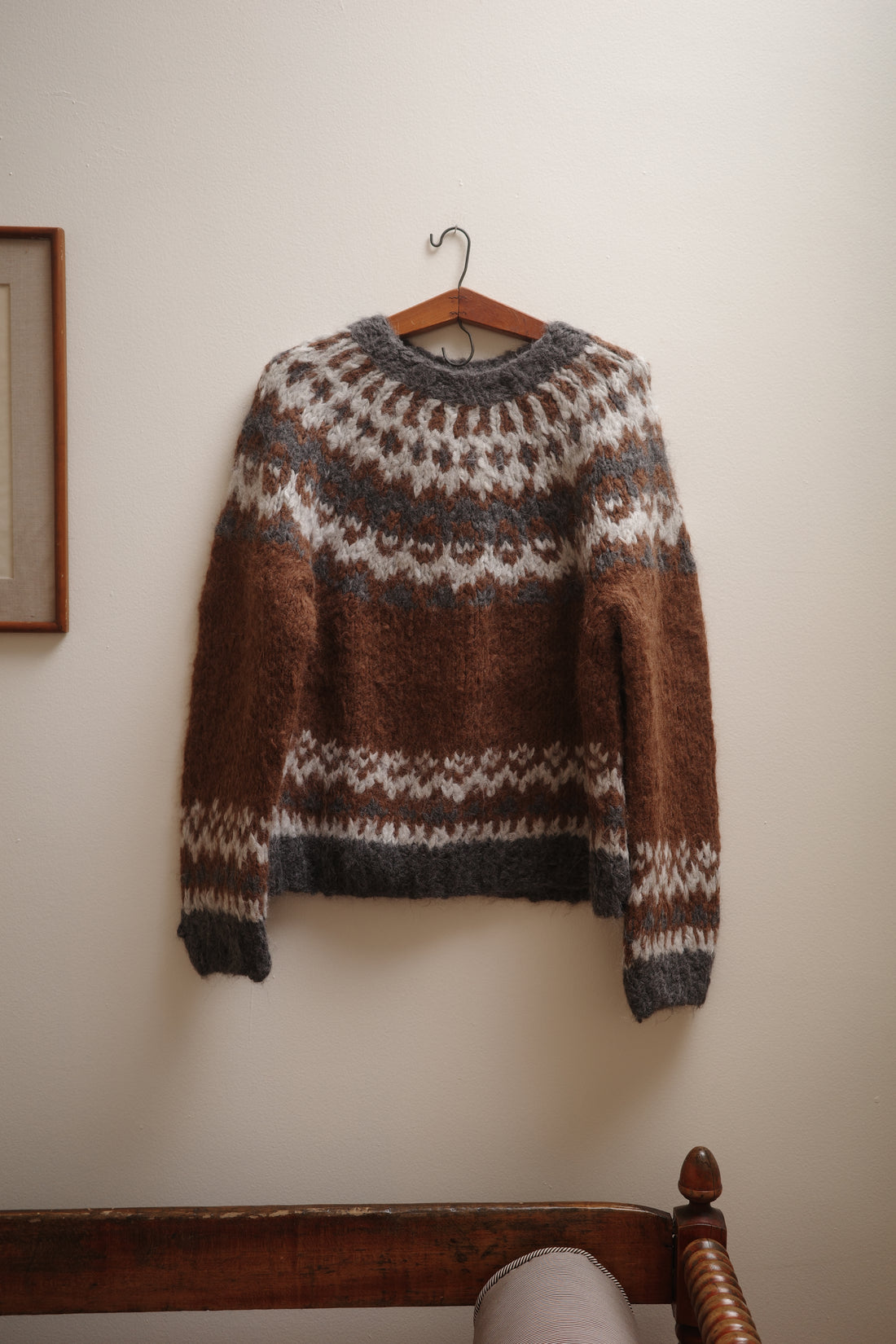 Brown and gray patterned sweater on a wooden hanger against a white wall.