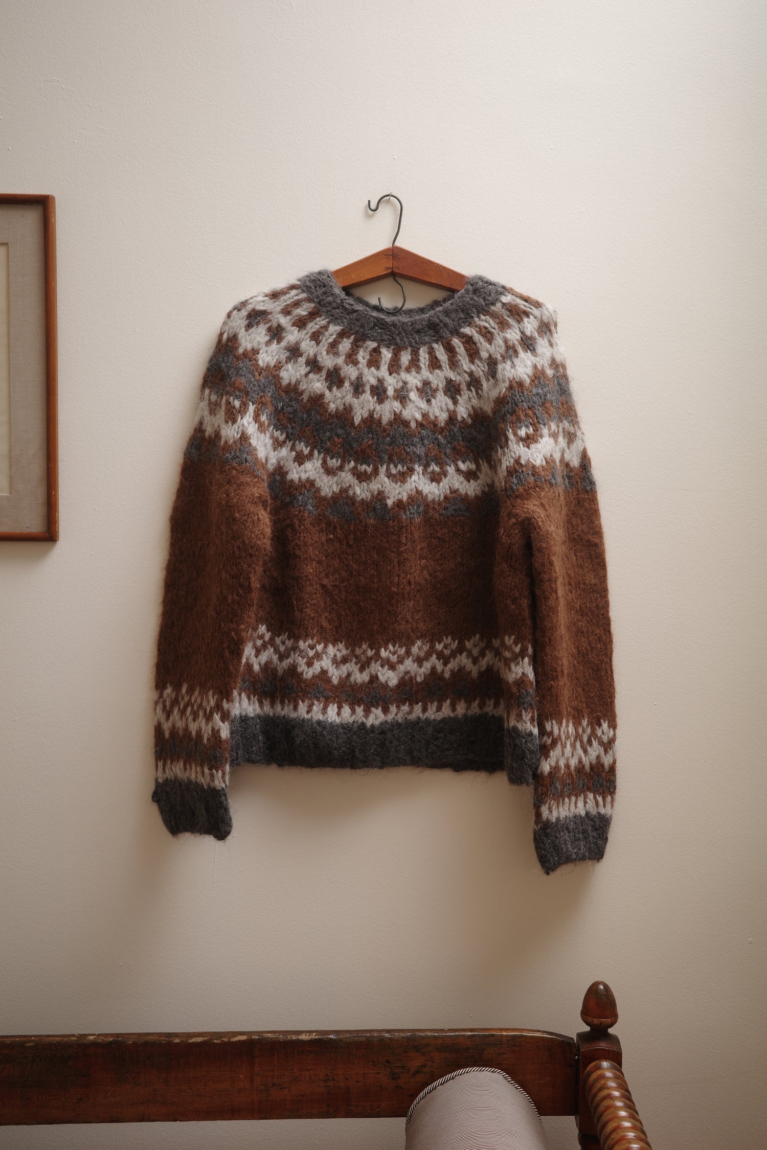 Brown and gray patterned sweater on a wooden hanger against a white wall.