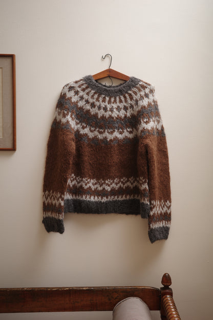 Brown and gray patterned sweater on a wooden hanger against a white wall.