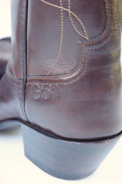 Close up image of the heel of a brown cowboy boot with embroidered stitching that reads &