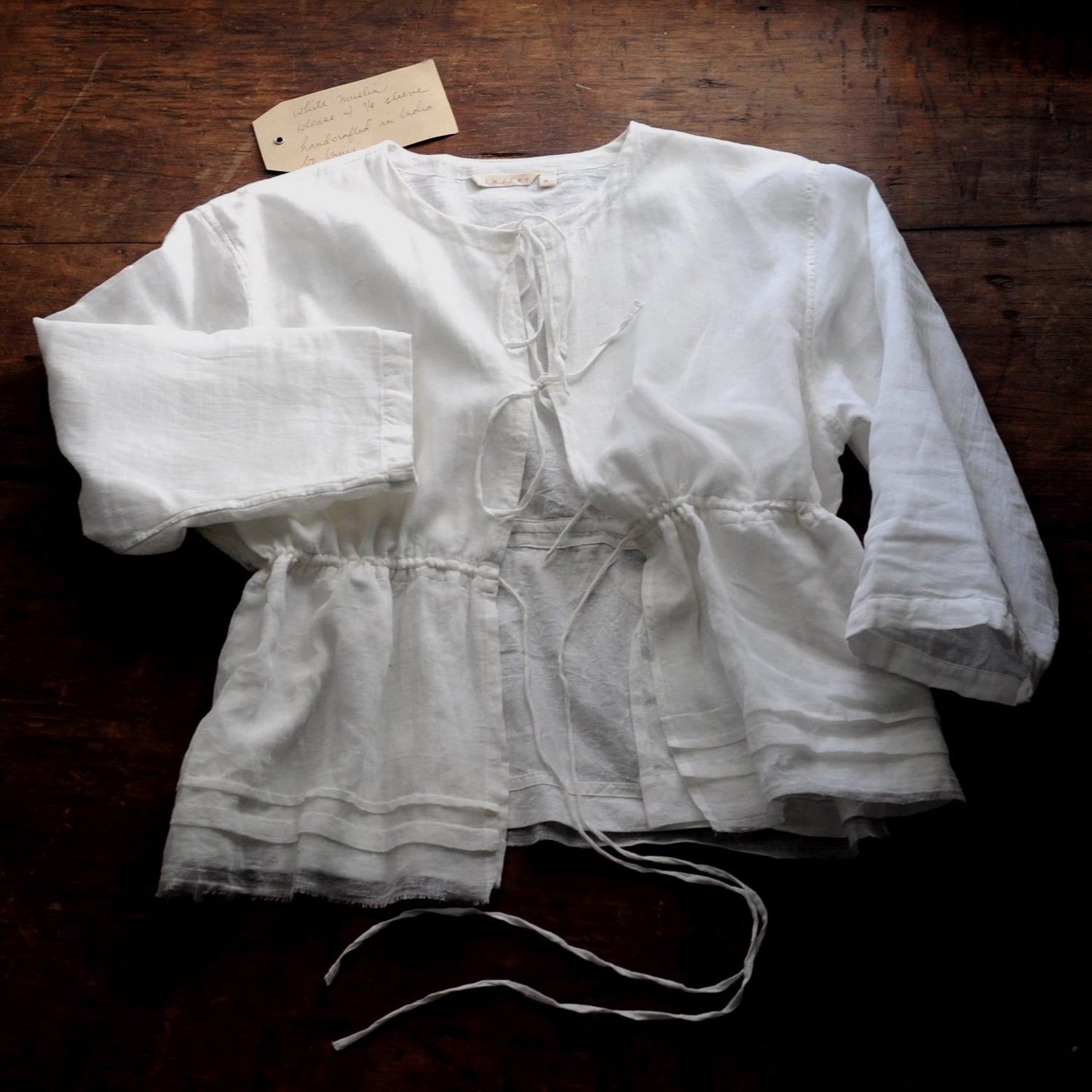 A white top with bow ties lays flat on top of a wooden table.