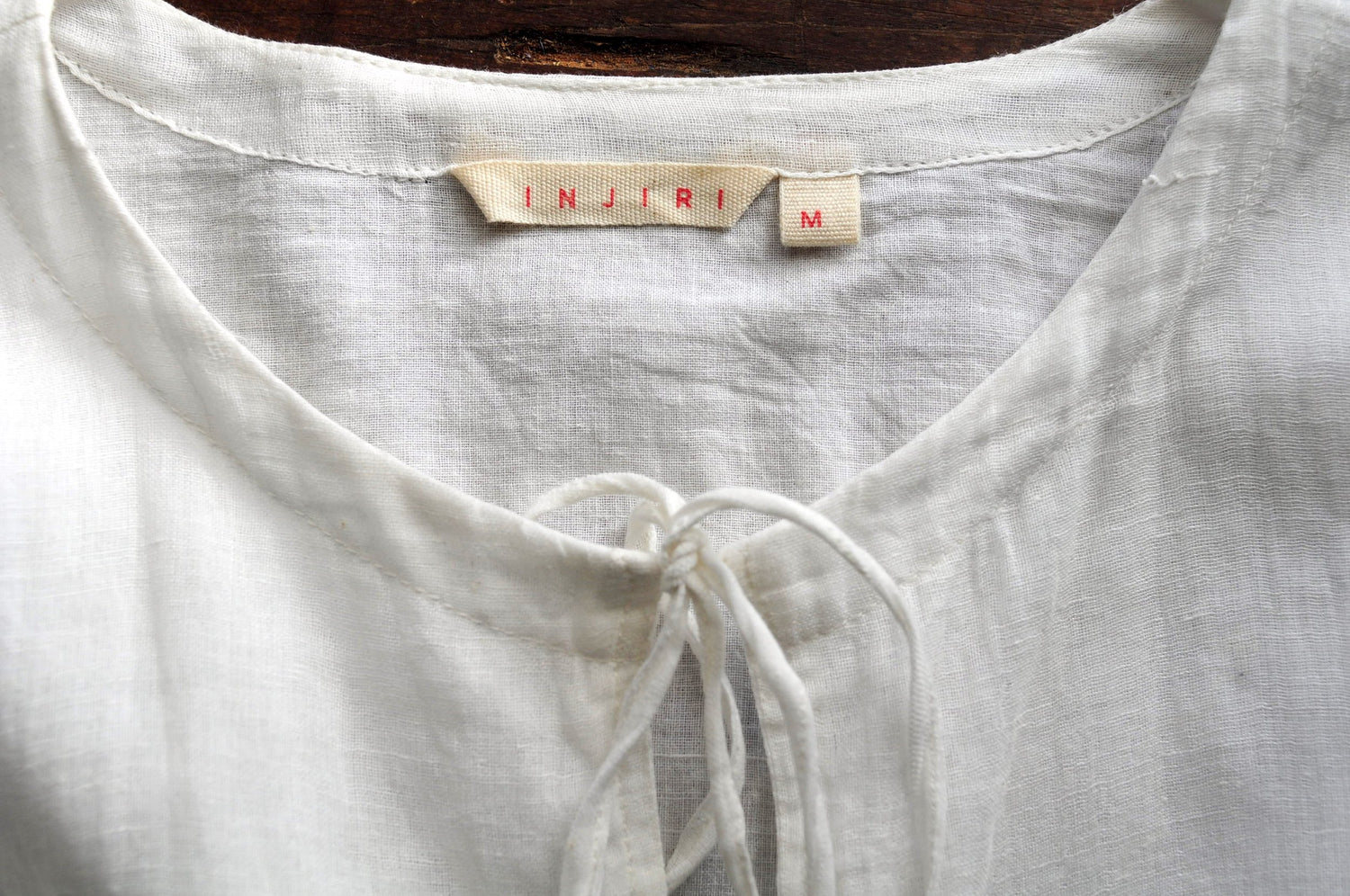 Close up image of the neck opening of a white chemise top with a label reading &
