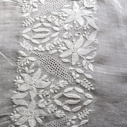 Close up image of white embroidered detailing on delicate white fabric.