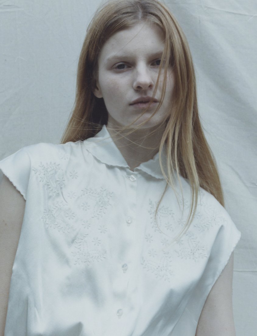 Blonde woman wearing a collared shirt with floral embroidery.