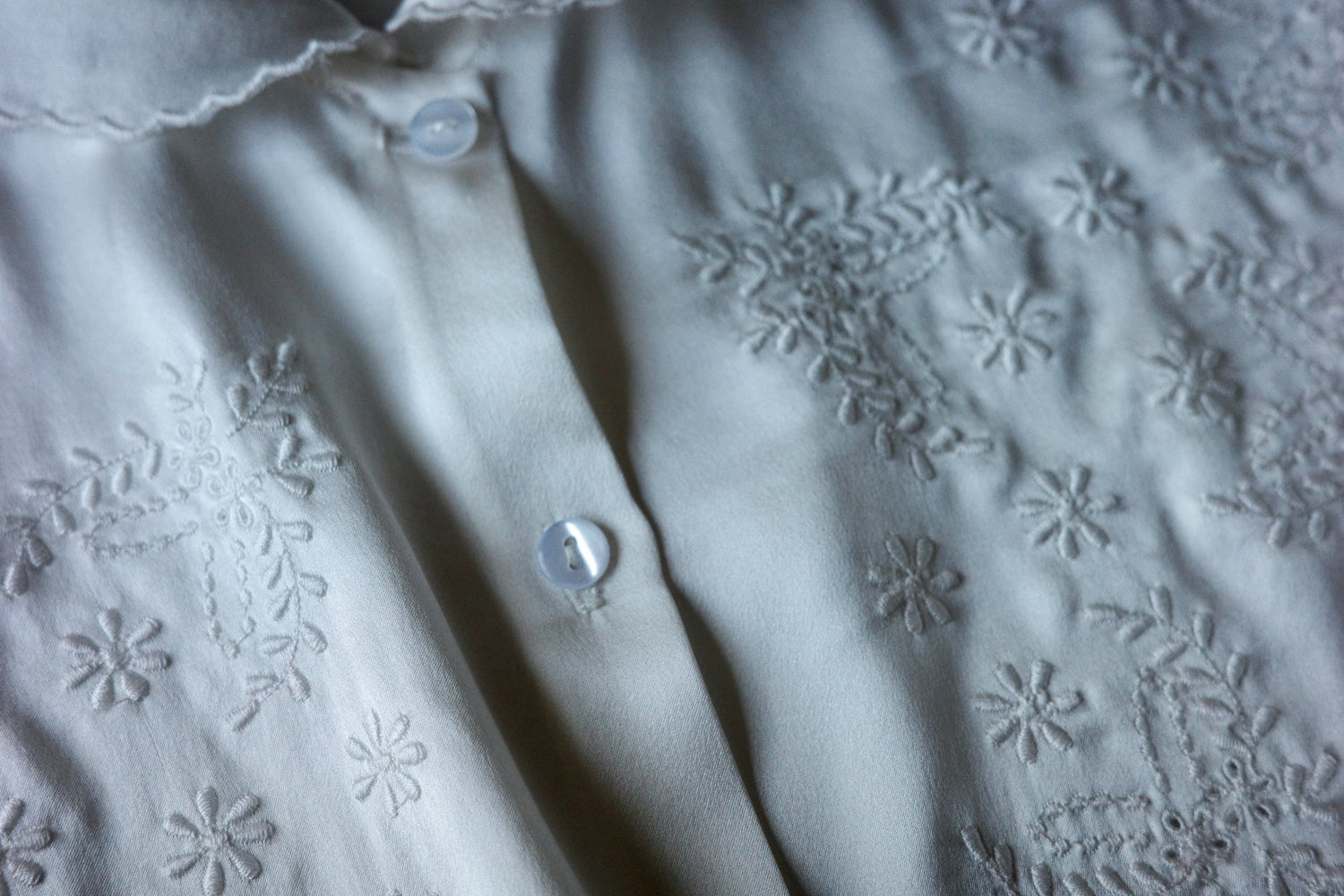 Detail shot of white button down shirt with floral embroidery.