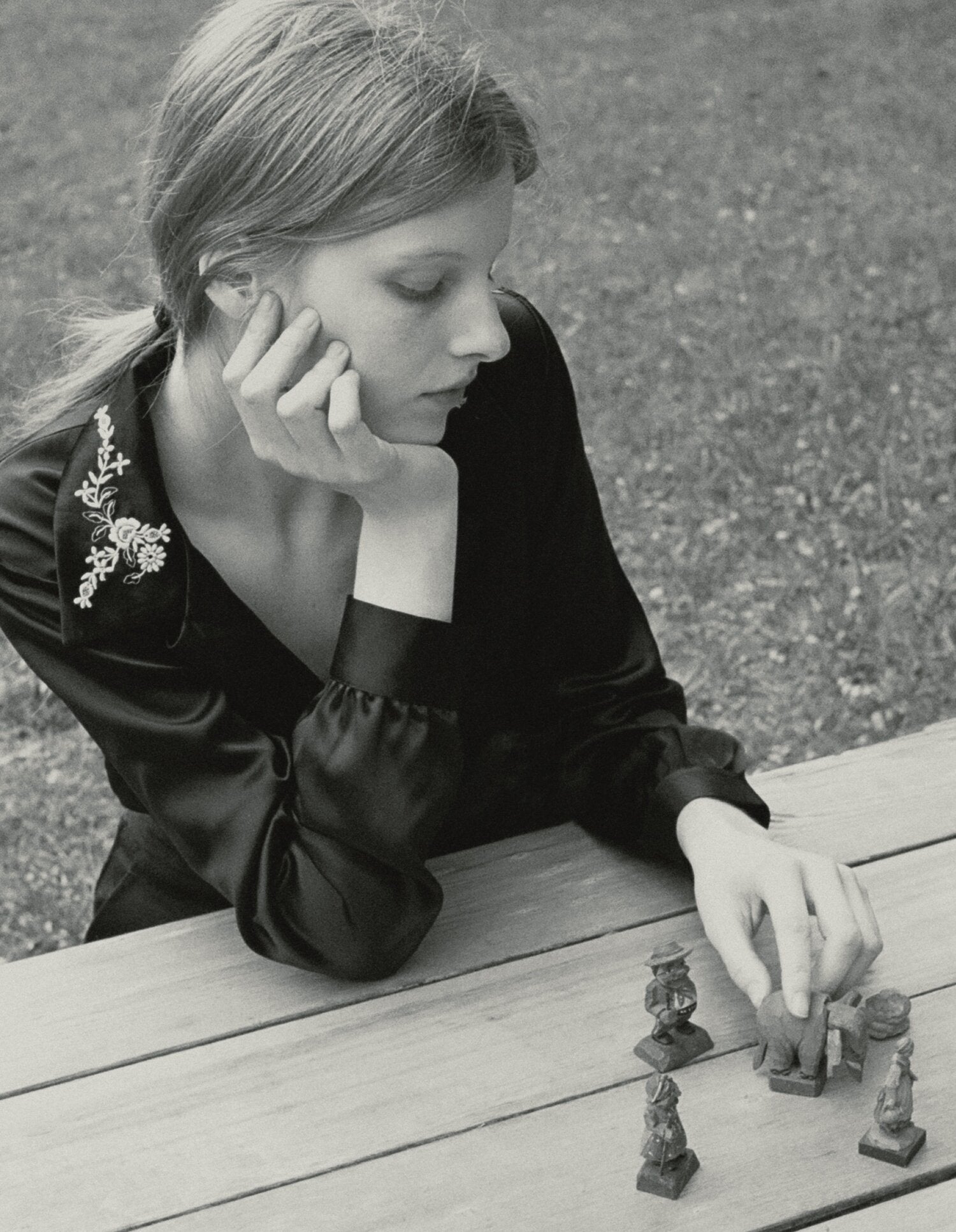 Black and white image of a model resting her chin on her hand wearing a black blouse