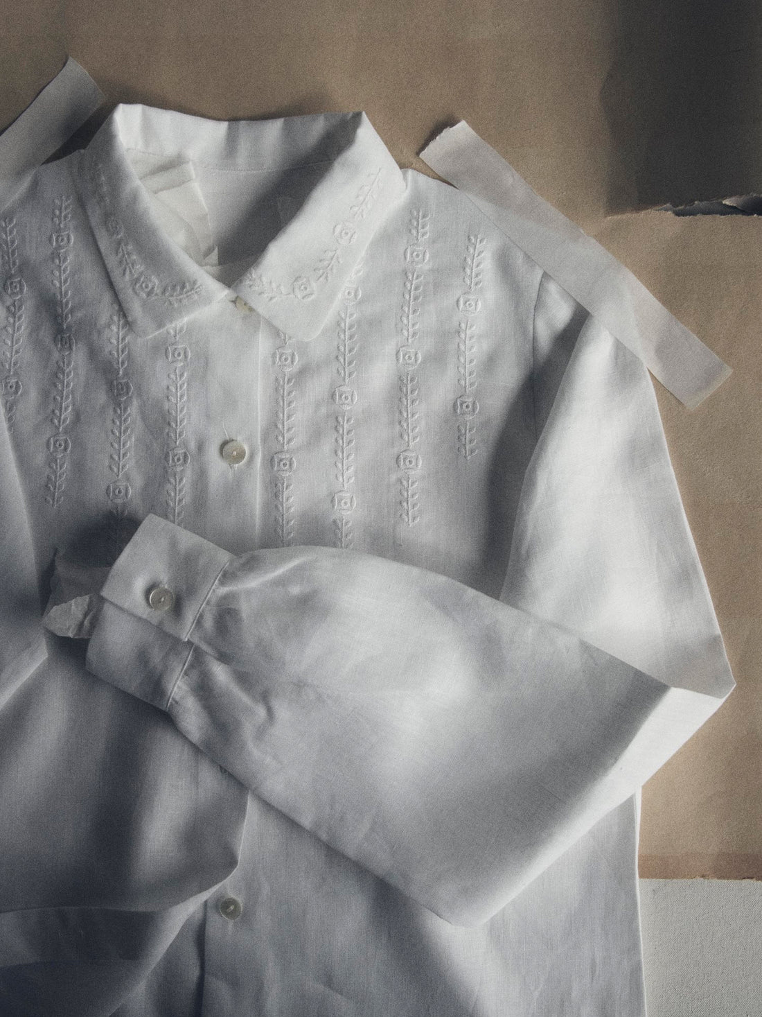 A white blouse with floral embroidery taped to brown paper.
