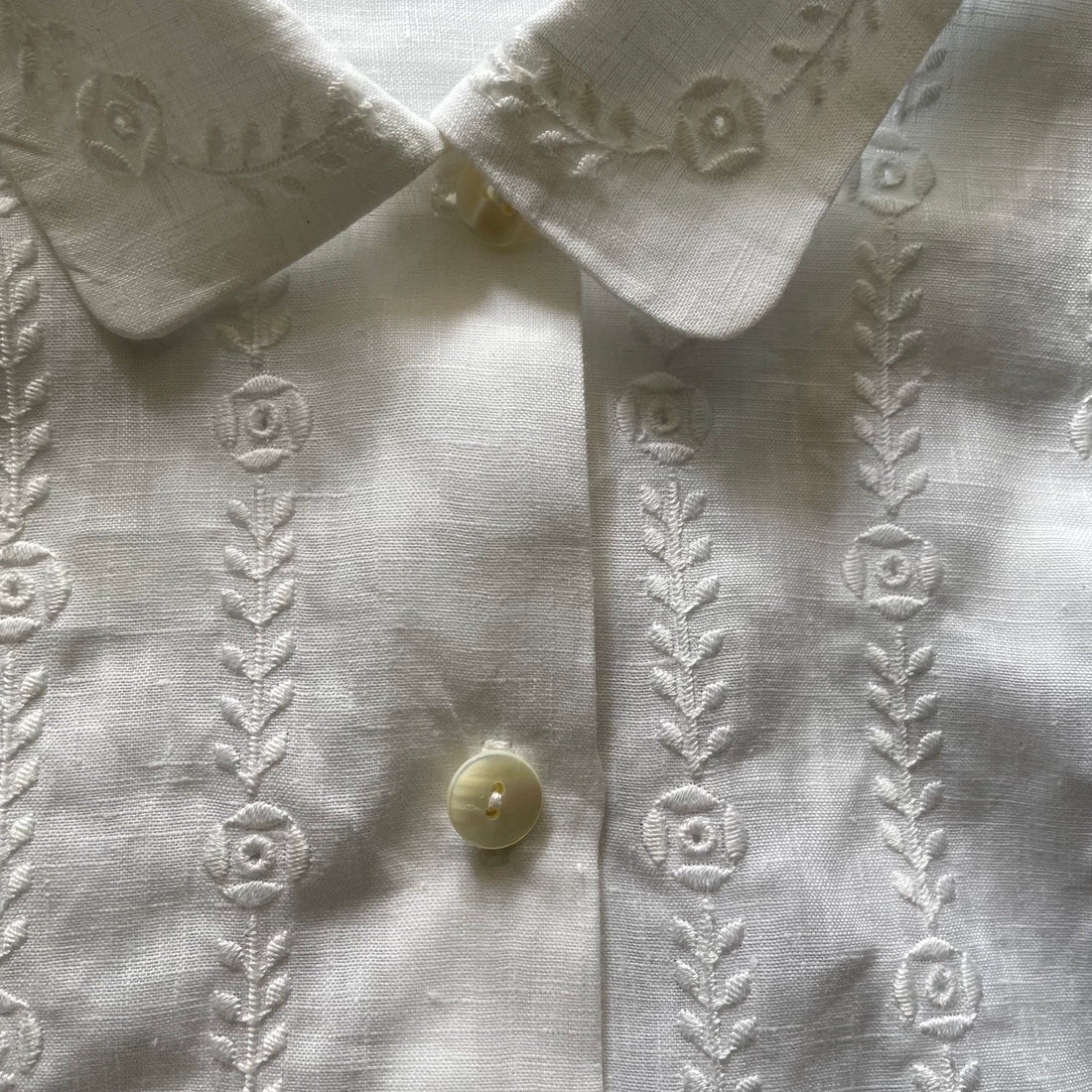 Close up image of floral embroidery on a white shirt with buttons and collar.