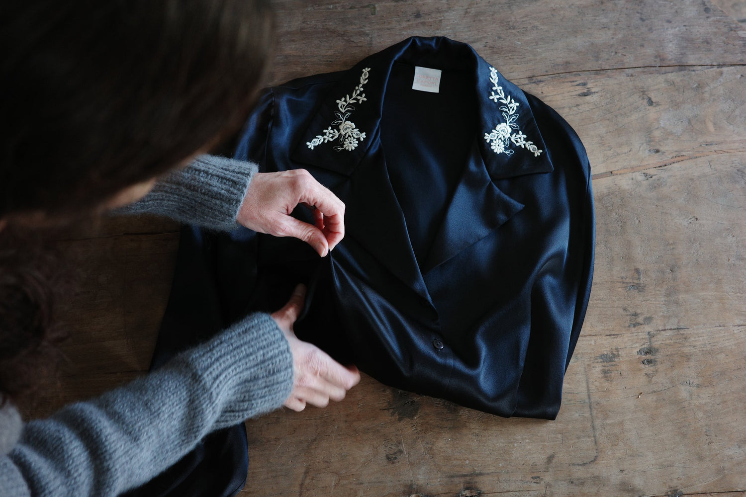 A woman adjusts a folded black shirt on top of a wooden table.