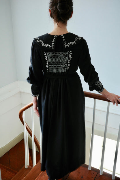 The back of a woman wearing a black dress with white embroidery.