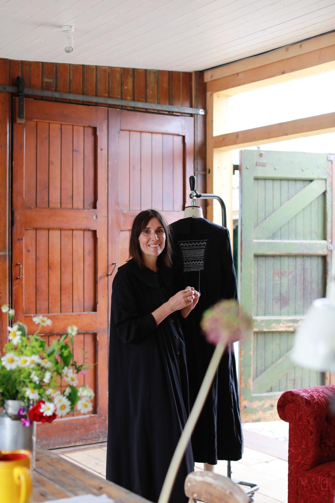 A woman smiles at the camera while standing in a room with wildflowers and wooden walls.