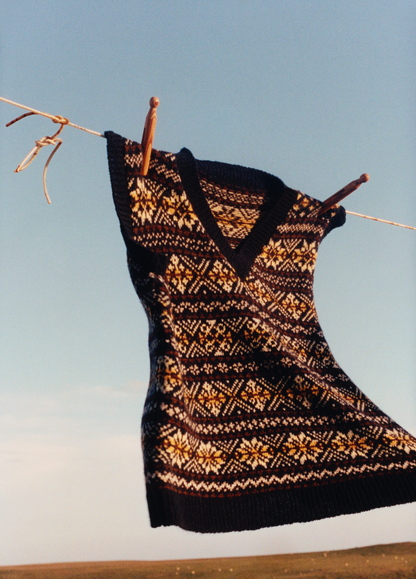 A traditional Fair Isle vest hanging on a clothesline against a blue sky.