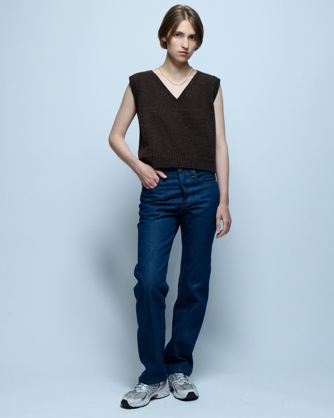 Model standing with her hand in her pocket wearing a brown vest and jeans.