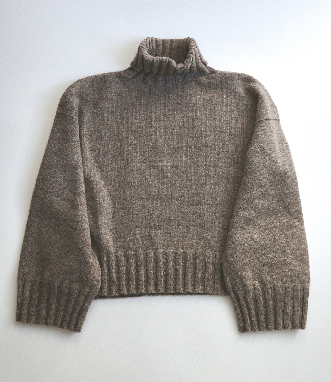 A grey turtle neck sweater lays flat on a white surface