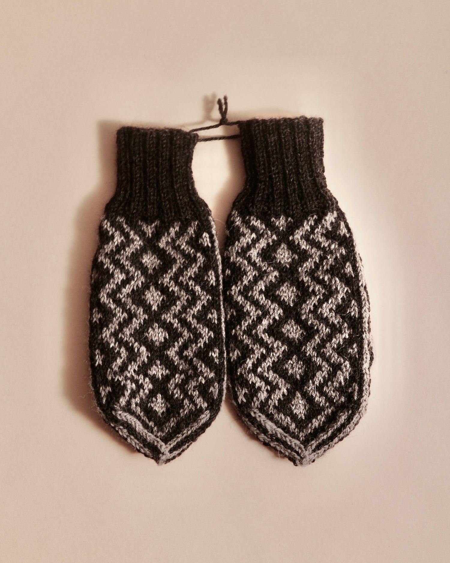 Pair of knitted mittens with a geometric pattern on a beige background