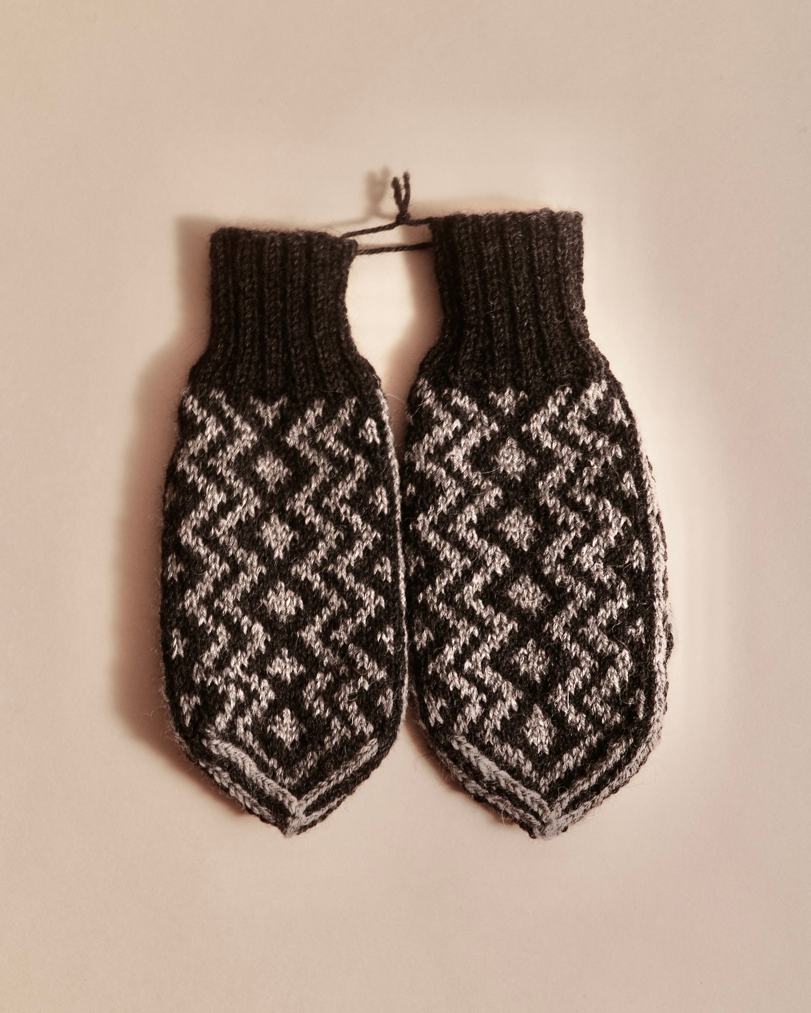 Pair of knitted mittens with a geometric pattern on a beige background