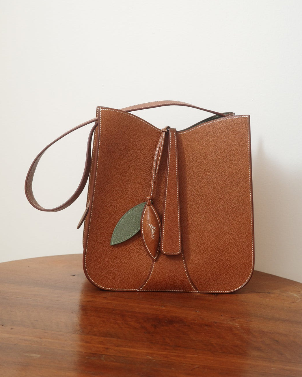 Brown leather handbag with a leaf detail on a wooden surface