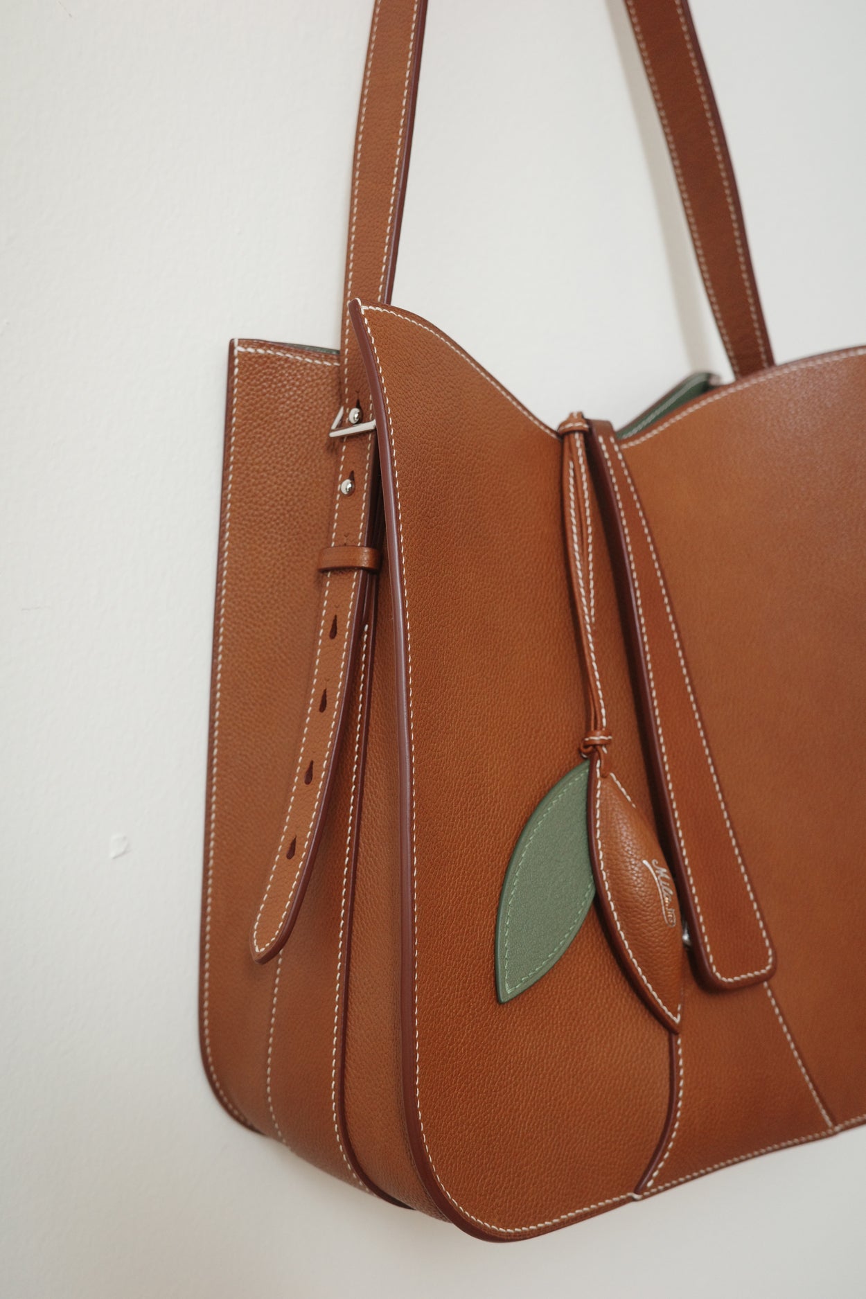 Brown leather handbag with a green leaf detail on a white background