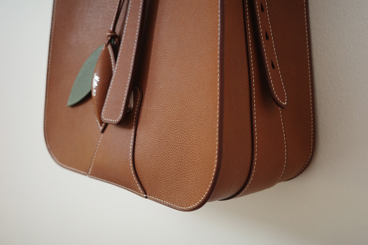 Brown leather bag with a green tag on a beige background