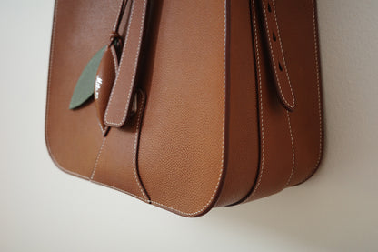 Brown leather bag with a green tag on a beige background