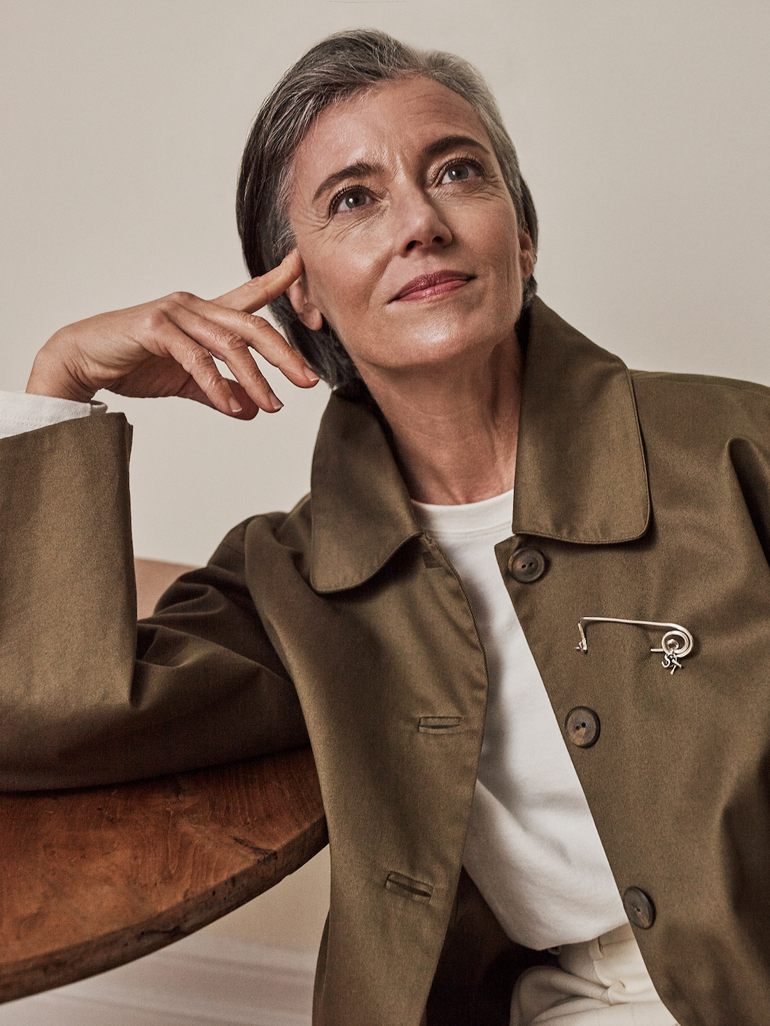 Woman wearing a brown coat with a brooch, sitting on a wooden surface.