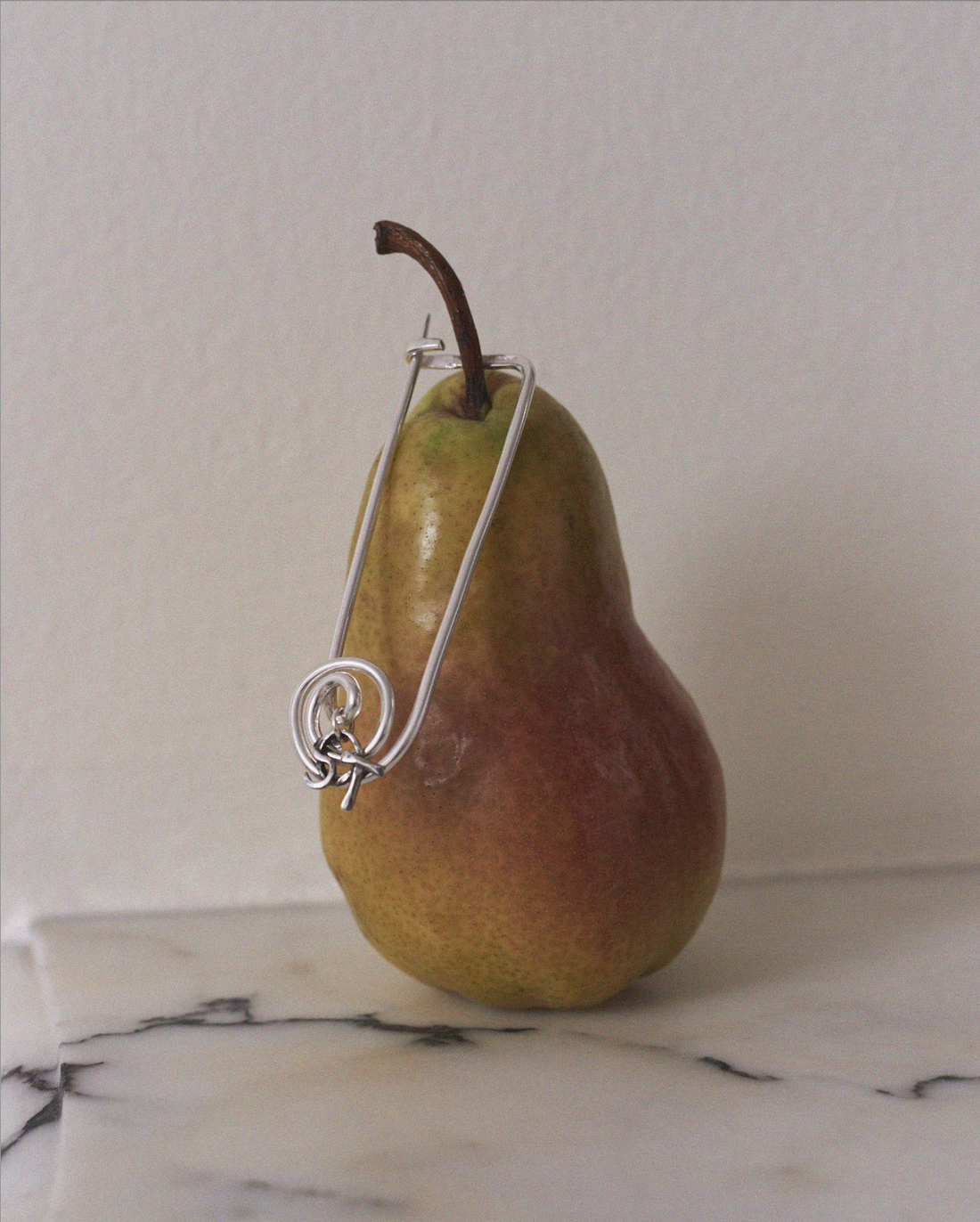 Pear with a silver wire wrapped around it on a marble surface