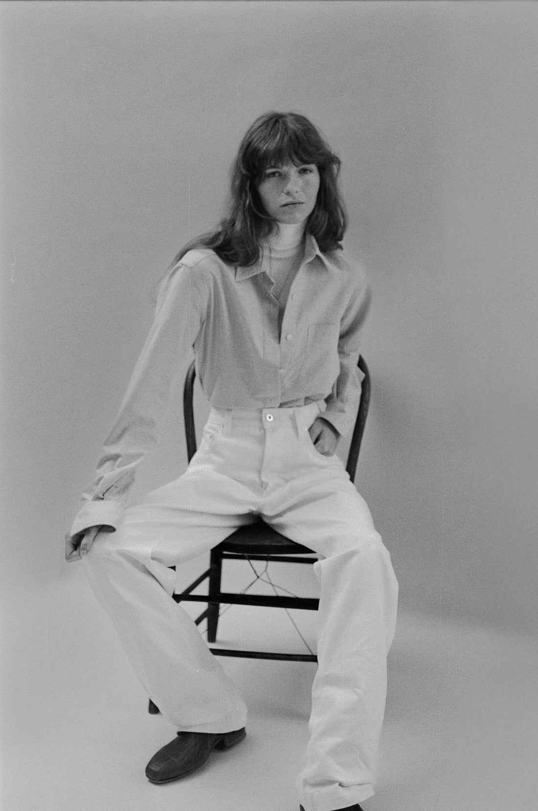 Seated Brunette woman wearing a white denim outfit against a plain background