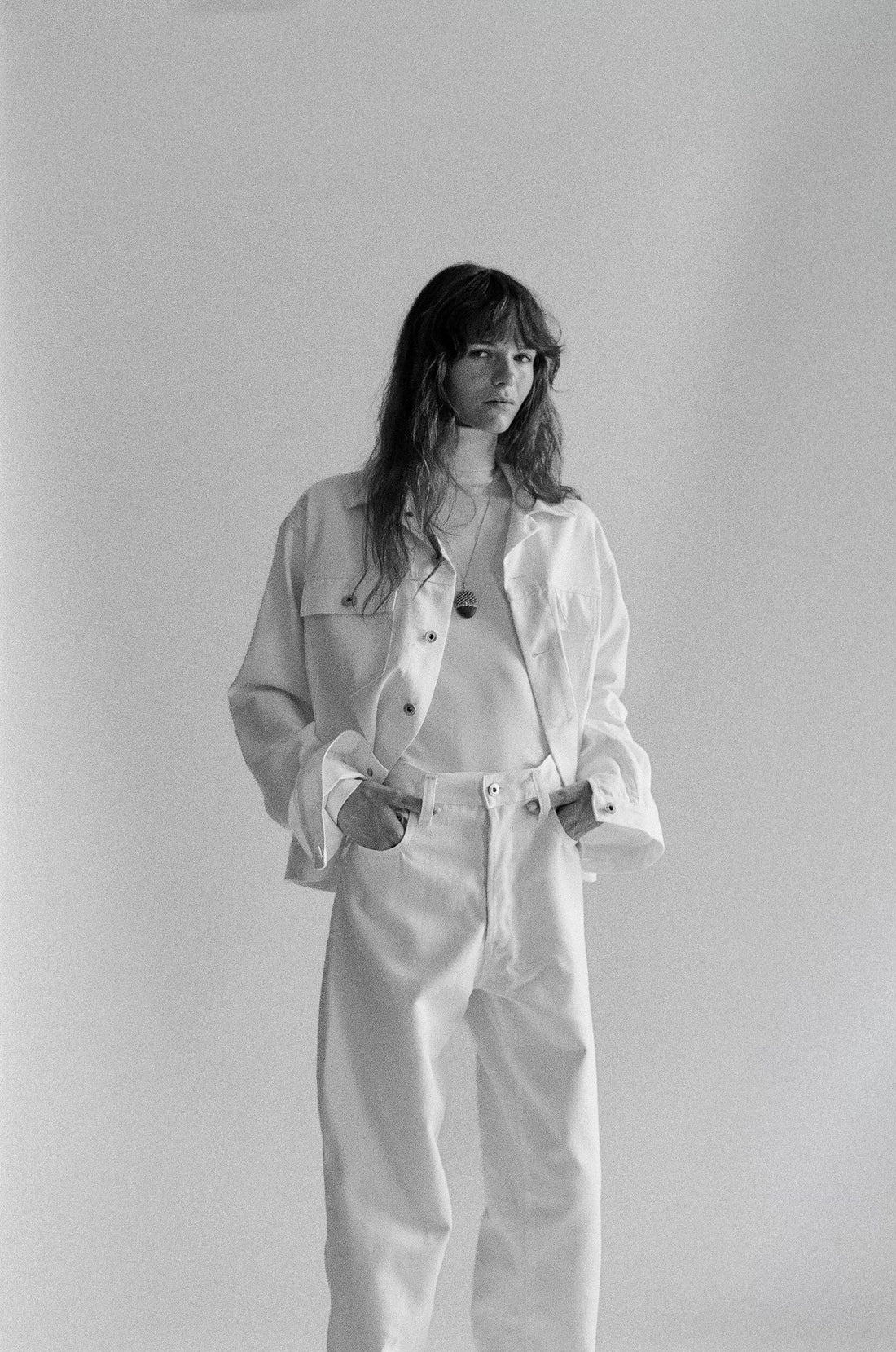Brunette woman wearing a white denim outfit against a plain background