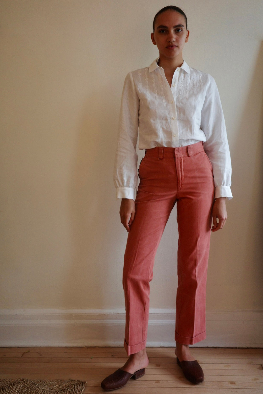 Woman standing in red trousers and white blouse against a wall