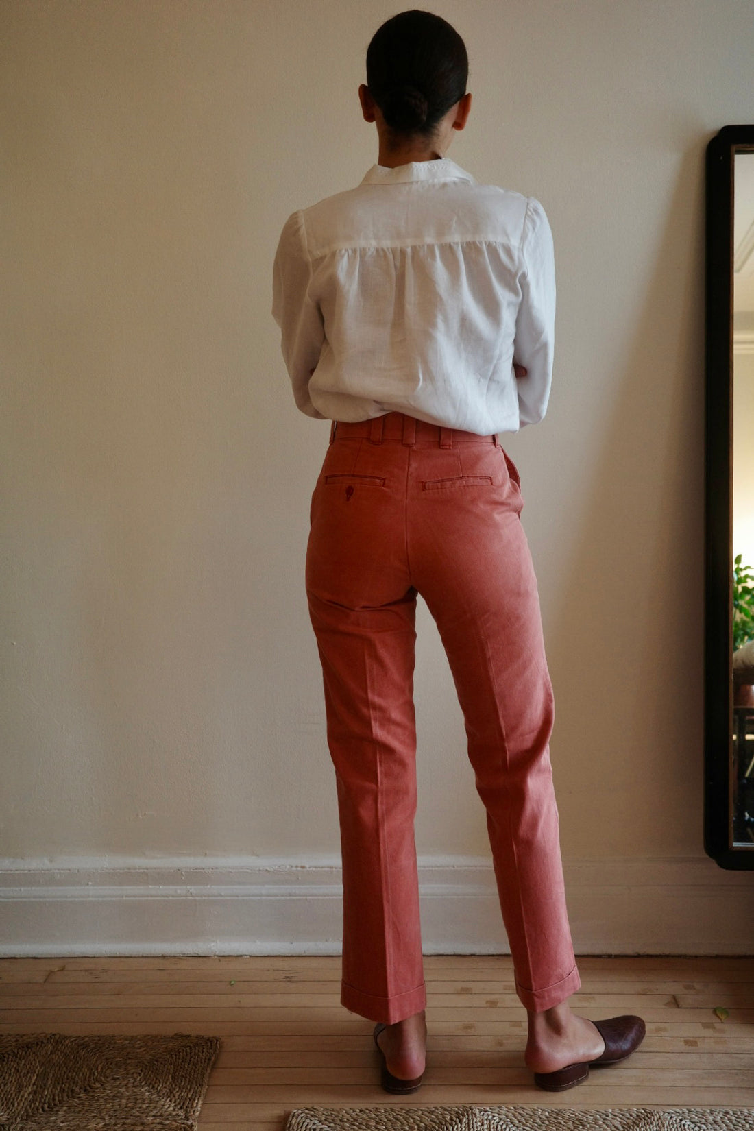 Woman standing with back to camera wearing red trousers and white blouse